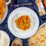 Served portion of halloumi, sweet potato and cauliflower curry in bowl with rice.