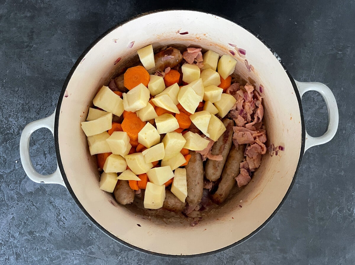sausages, bacon, carrots and sweet in cast iron cooking dish.