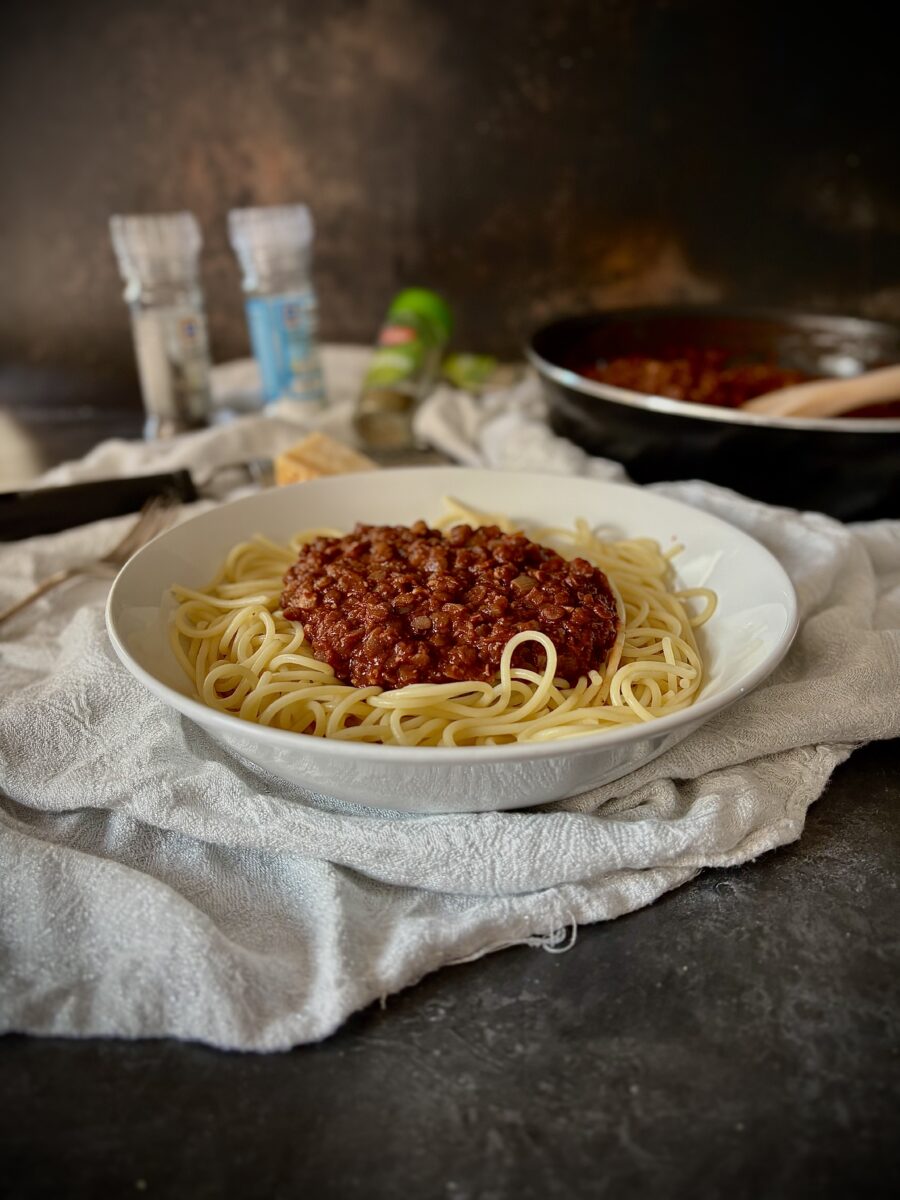 Bowl of vegetarian bolognese with spaghetti, cooking pan in the background.