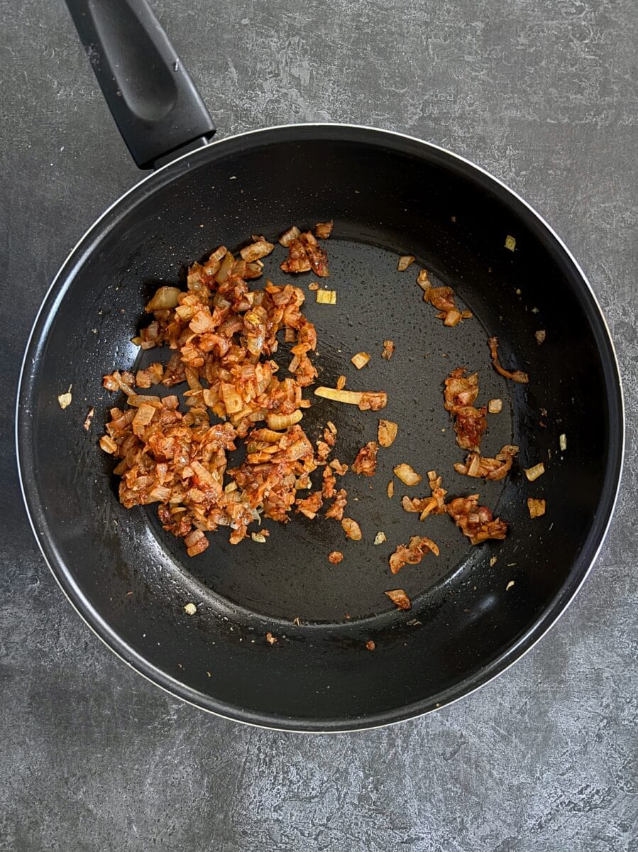onions in tomato puree frying in a pan.