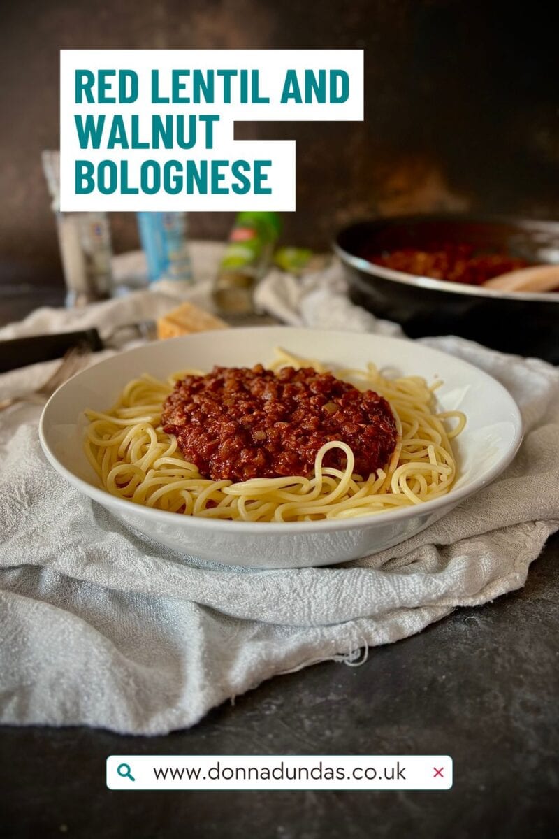 Bowl of vegetarian bolognese with spaghetti, cooking pan in the background.